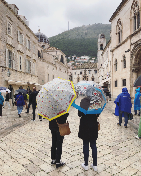 Sheridan and Lucy standing with their back to the camera, holding umbrellas in teh old town of dubrovnik