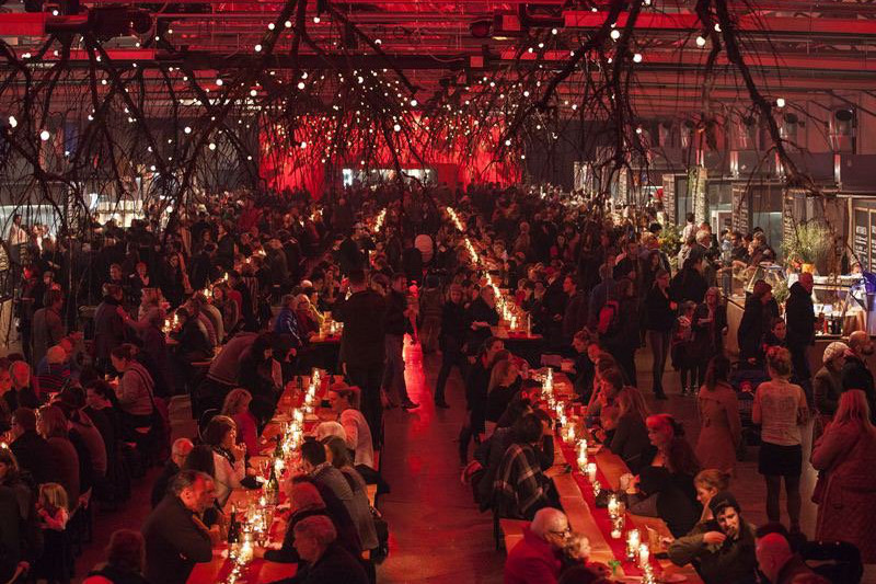 Large hall filled with people at communal dining tables.