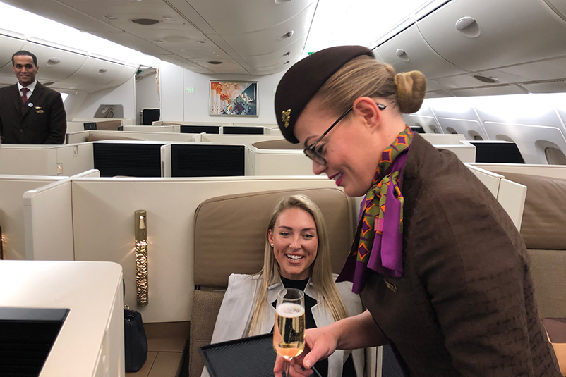 A flight attendant serves a glass of champagne to a female passenger