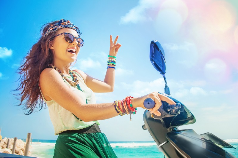 A woman riding a motorbike along beach that should be wearing a helmet!
