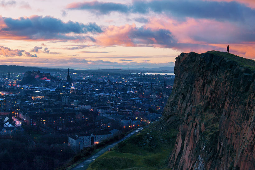 man ontop of arthurs peak overlooking edinburgh at sunset