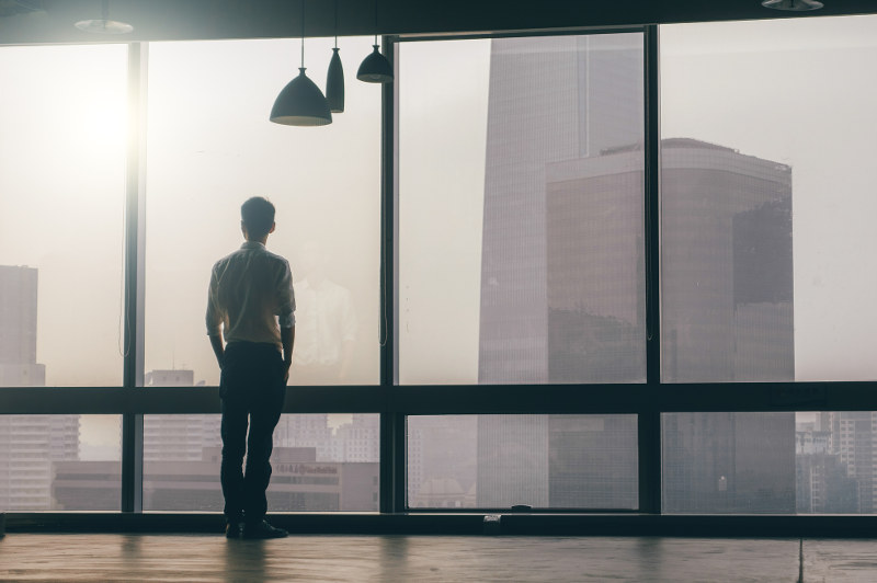 man looking out office window over city