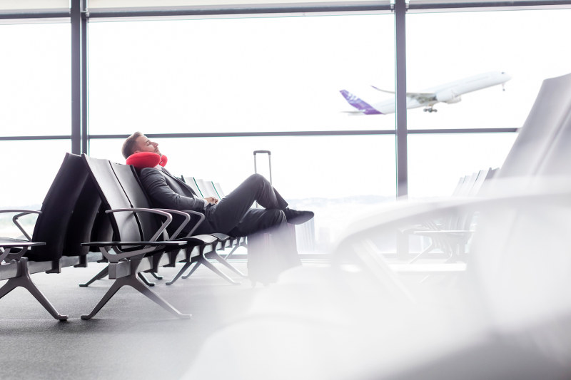 man sitting with travel pillow in airport lounge
