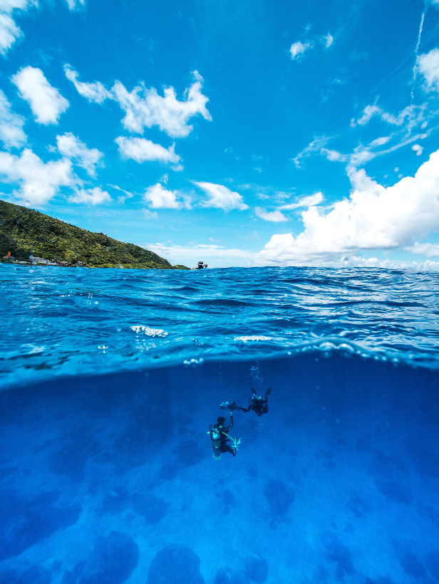 divers under water with view of ocean and mountains above