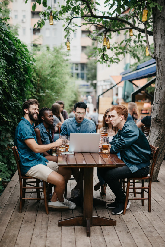 group sitting around laptop at table with beers in europe