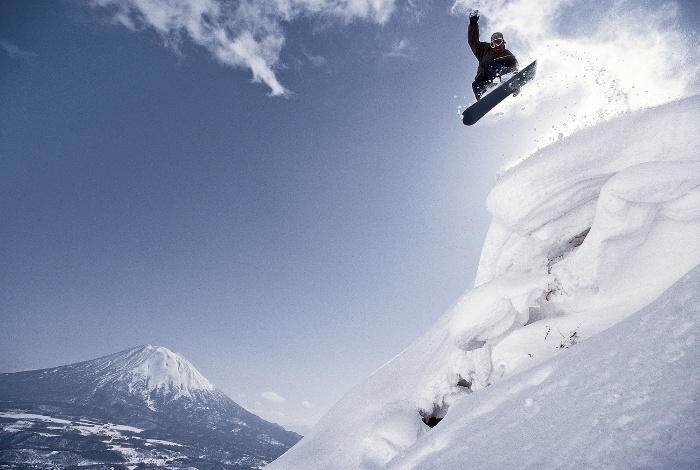 snow boarder jumping off mountain with mount fuji behind