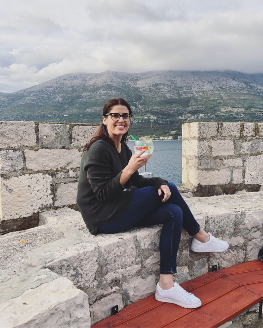 Sheridan sitting on the tower, holding a big gin and tonic. Views of the mountains and sea behind her