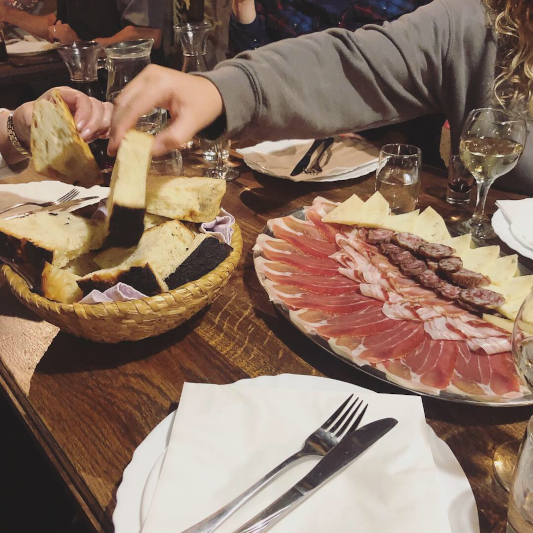 homemade bread, cured meat on a set table. A hand is reaching for the bread