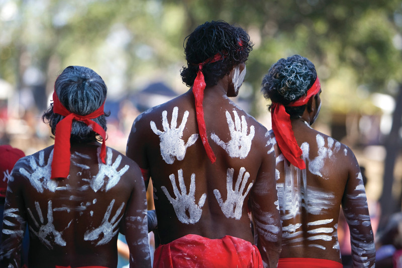 Aboriginal dancers seen from behind with white ochre hand-prints on their backs.