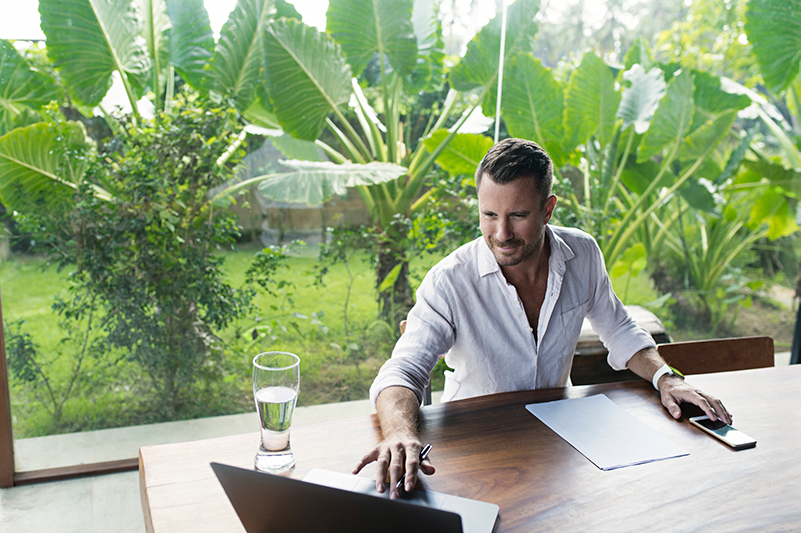 Man works on a laptop with a garden backdrop in Bali