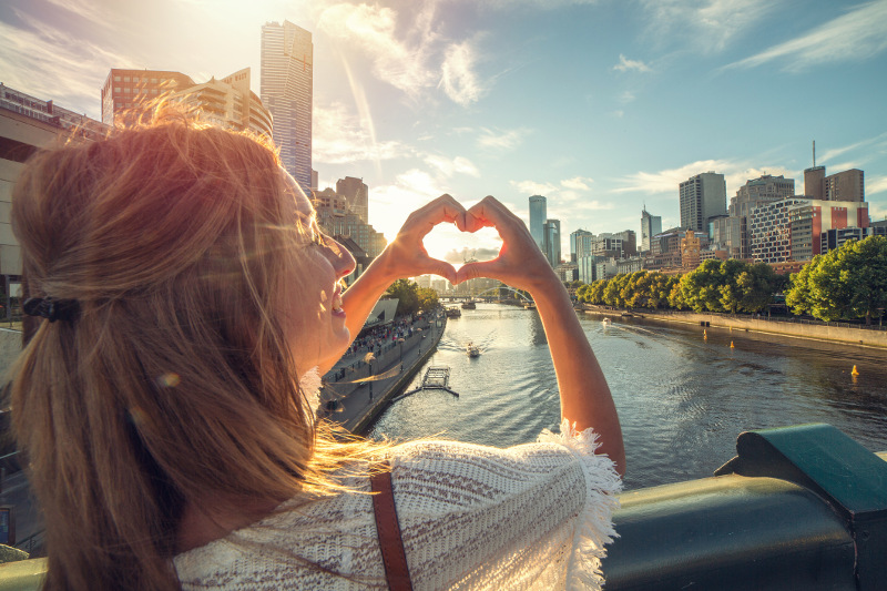 A girl making a loveheart with Melbourne city in the background