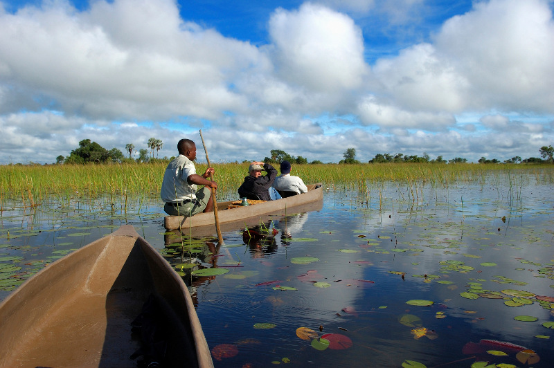 Three people in a traditional dug-out canoe on the Okavango Delta, Botswana