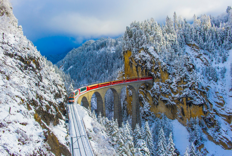 Red train crosses Landwasser viaduct Switzerland in winter