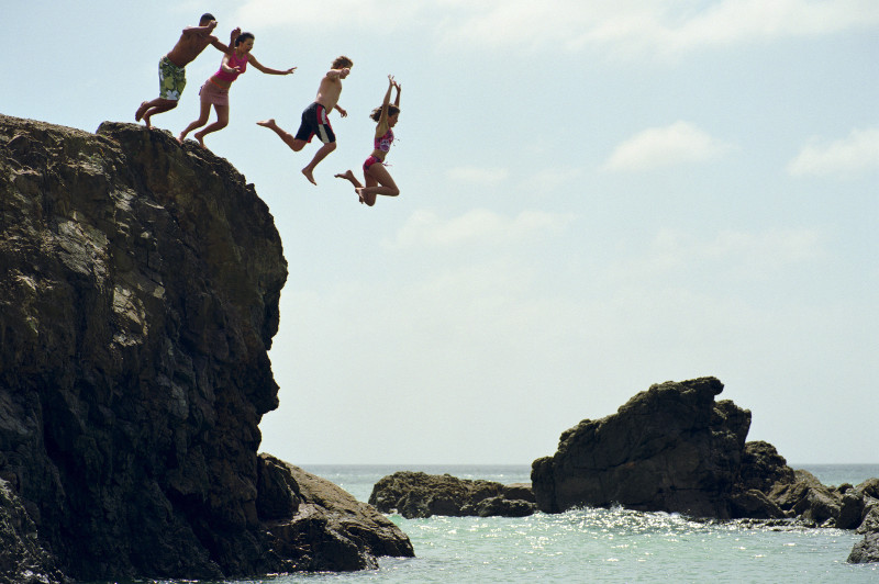 Friends leap off rock at Te Arai Point, North Island, New Zealand.