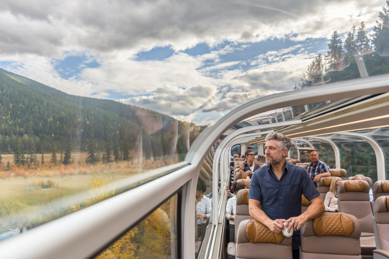 man on rocky mountaineer train looking out clear dome