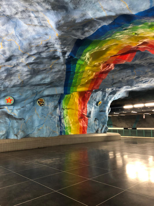 A photo of an underground station in Stockholm, with a painting of a rainbow on the walls