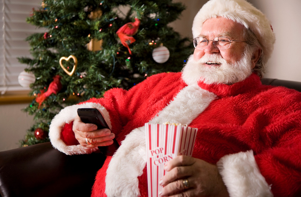 Santa watching a movie holding a remote and popcorn