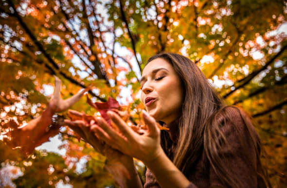 A woman plays with Autumn leaves.