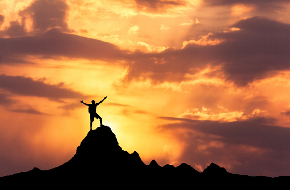 A man stands on a mountain in the glow of sunrise.