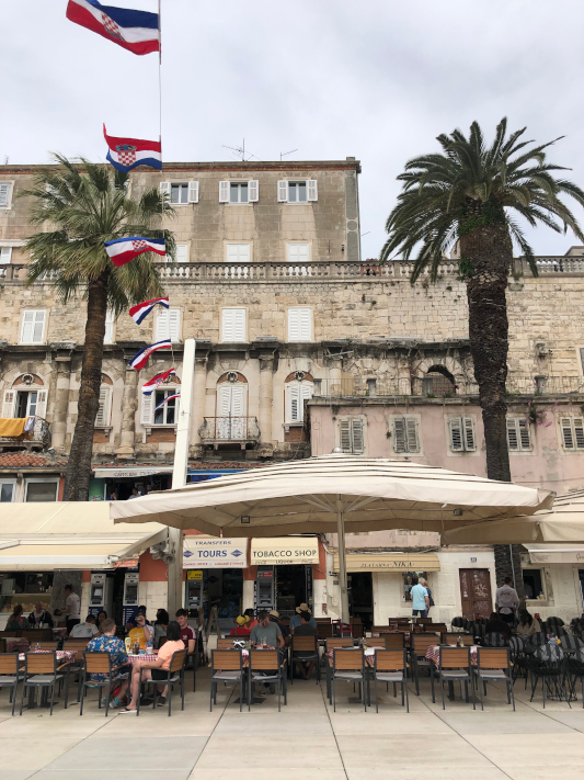 Split promenade with cafe chairs sitting outside the restaurants. Old ruins tower above ground level
