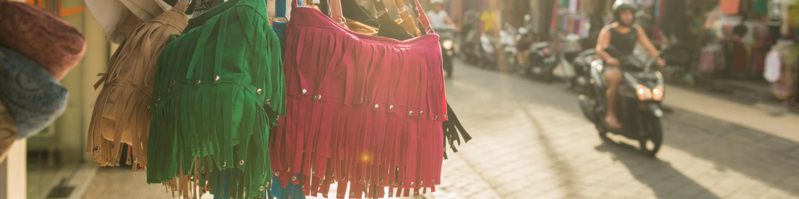 handbags hanging at a market and motorbike in background