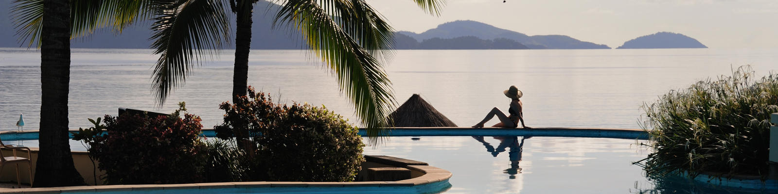 Woman sitting on the edge of the pool at a beachfront resort as the sun goes down at Hamilton Island.
