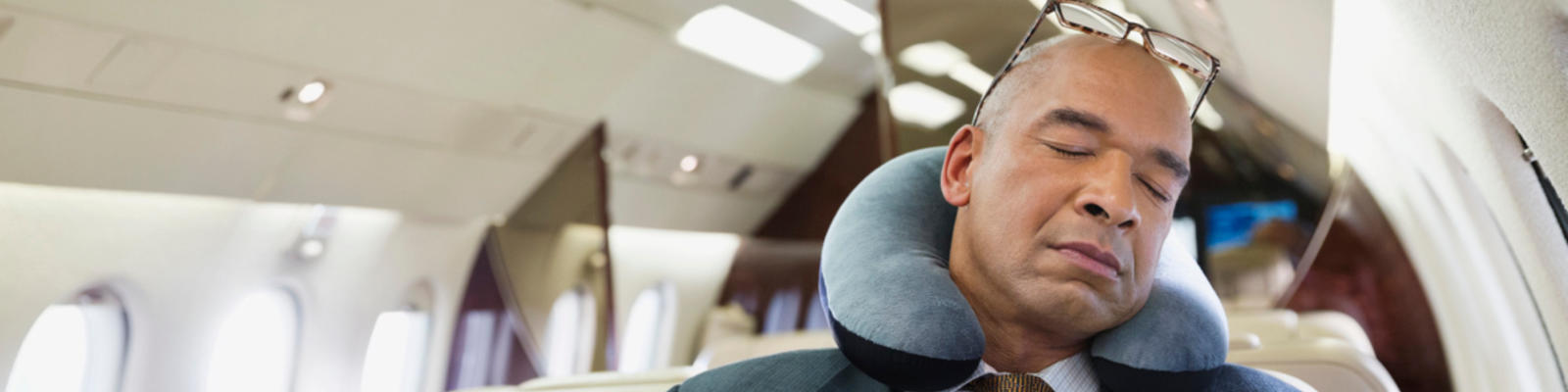 A man sleeping on a plane with a neck pillow around his neck
