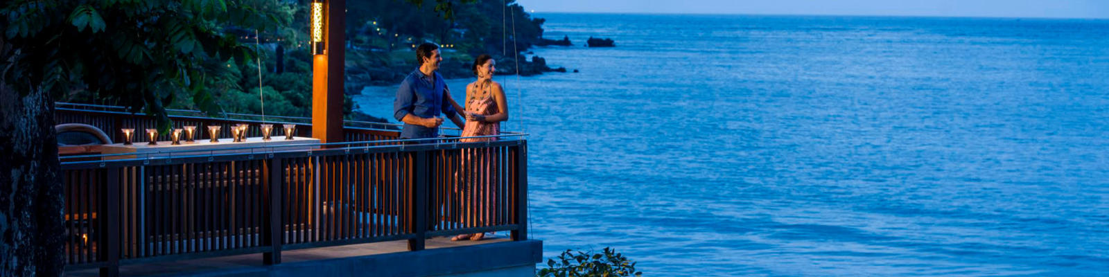 Two people standing on a balcony with drinks overlooking the ocean
