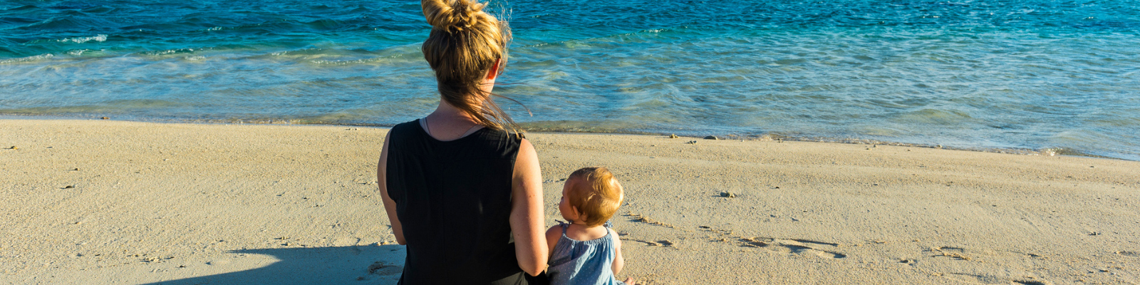 A woman and baby sit looking out to sea from a beach in Rarotonga