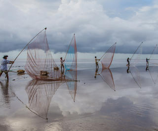 Fisherfolk cast their nets on a beach at the Mekong Delta in south Vietnam