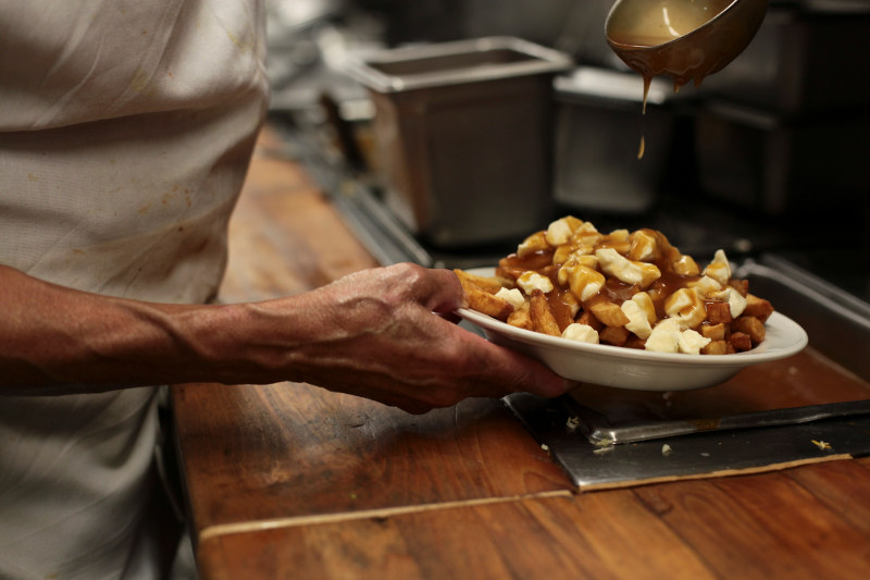 A cook pours gravy on a dish of poutine.