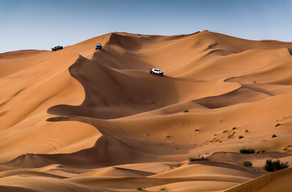 Four-wheel-drives zoom down dunes in the Dubai desert.