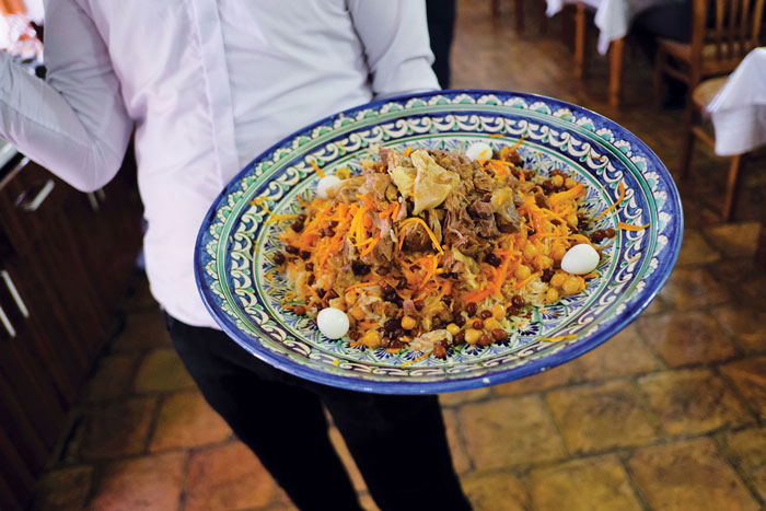 a waiter carries a plate of plov, a combination of lamb, rice, onion and carrots