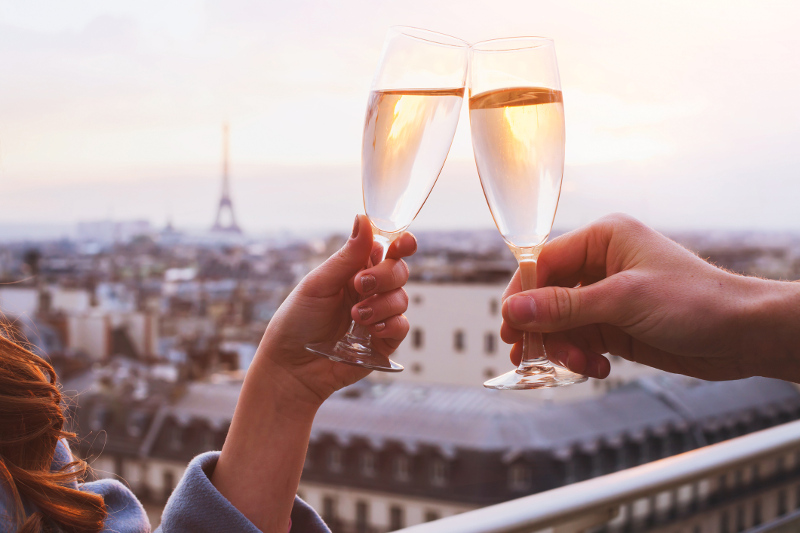 A couple of glasses of Champagne being clinked with the Eiffel Tower in the background.