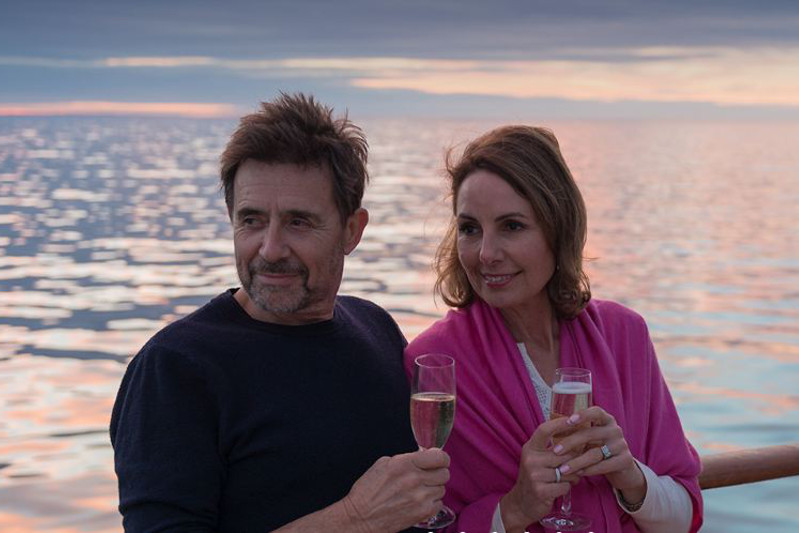 Man and woman holding champagne while leaning on the balcony.